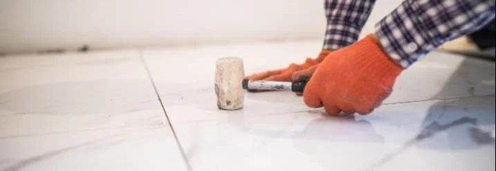 Person verlegt Fliesen mit Gummihammer